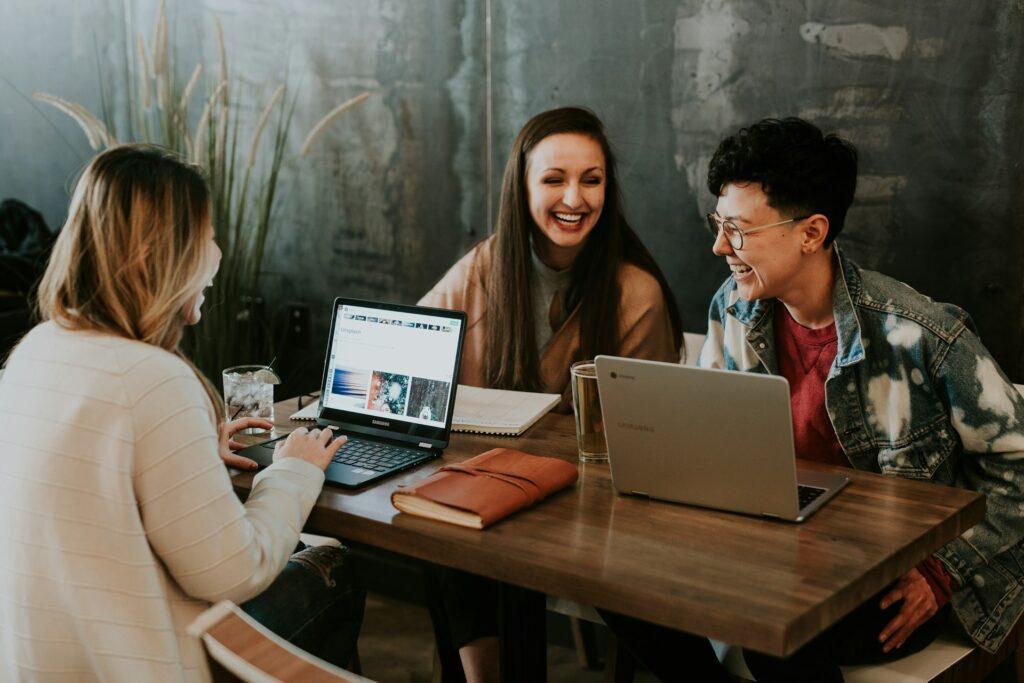 Drei Personen arbeiten lächelnd an Laptops und besprechen ein Projekt, Teamarbeit in der Internetagentur aus Düsseldorf