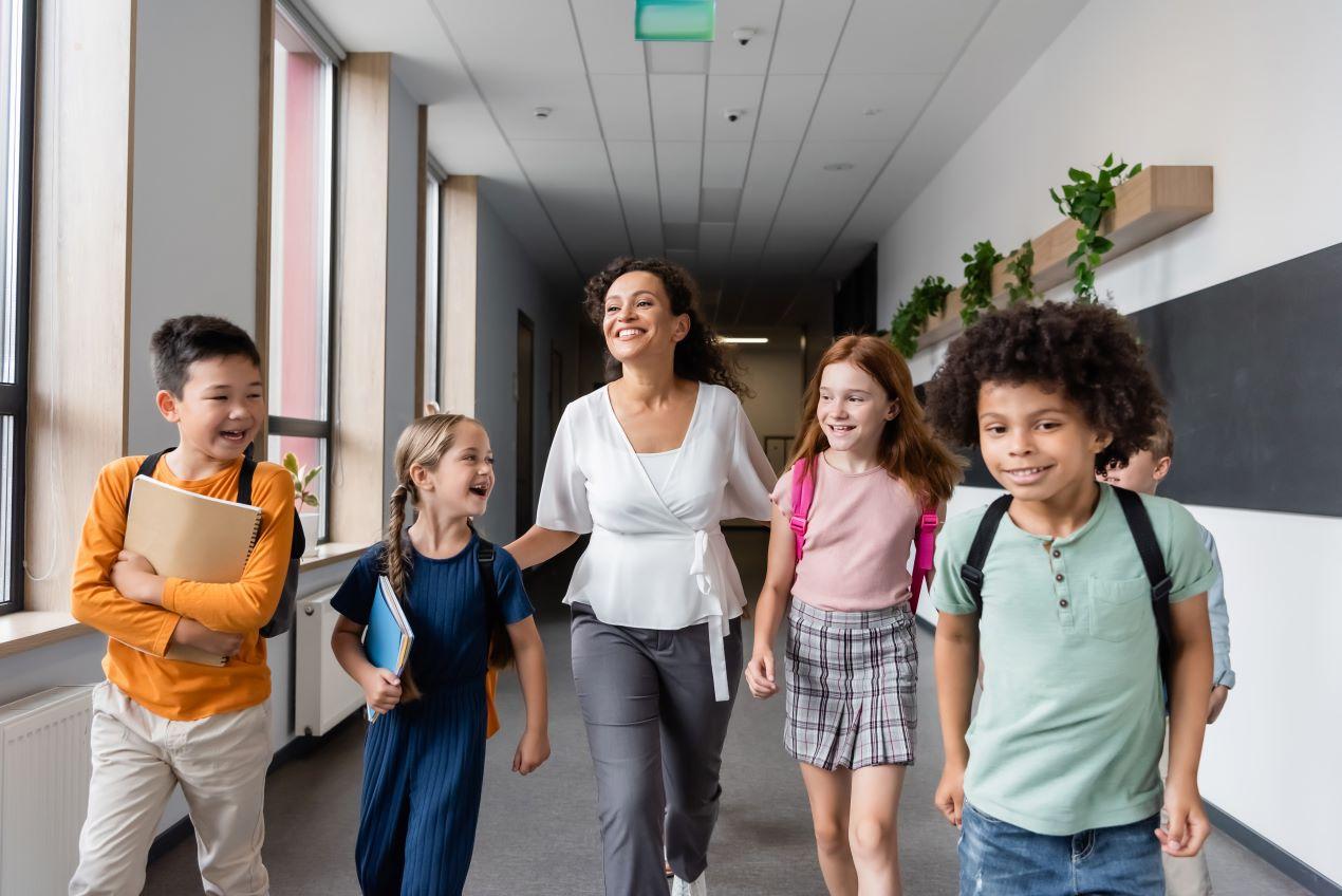 Lehrerin mit einer diversen Gruppe von Grundschulkindern im Flur – Berlin bilinguale Grundschule für multikulturelles Lernen