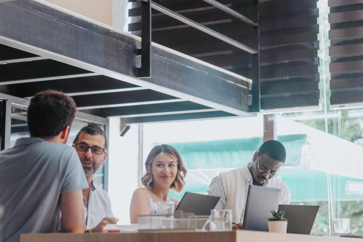 Team von vier Personen in einem modernen Büro, arbeitet mit Laptops und diskutiert Strategien, repräsentiert die Zusammenarbeit mit einer Social Media Agentur