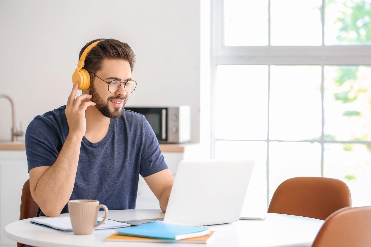 Mann mit gelben Kopfhörern, der an einem Laptop arbeitet, während er an einem E-Learning-Kurs zum Thema Hygiene teilnimmt.