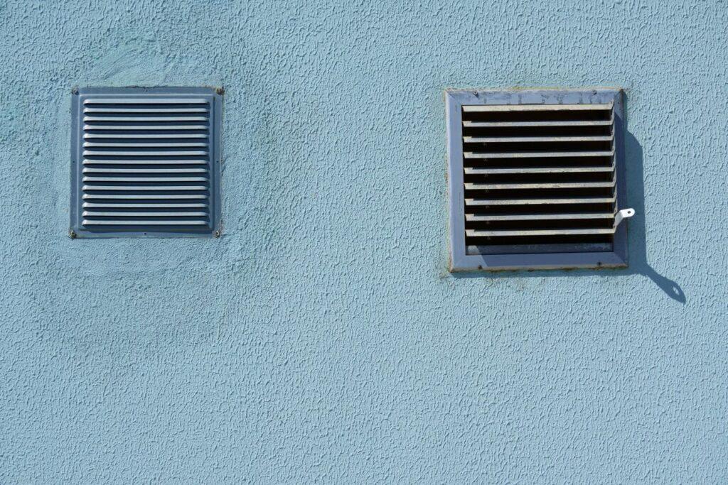 Zwei Wetterschutzgitter aus Metall an einer blauen Putzfassade – sorgt für Luftzirkulation und schützt vor Regen, Schmutz und Insekten